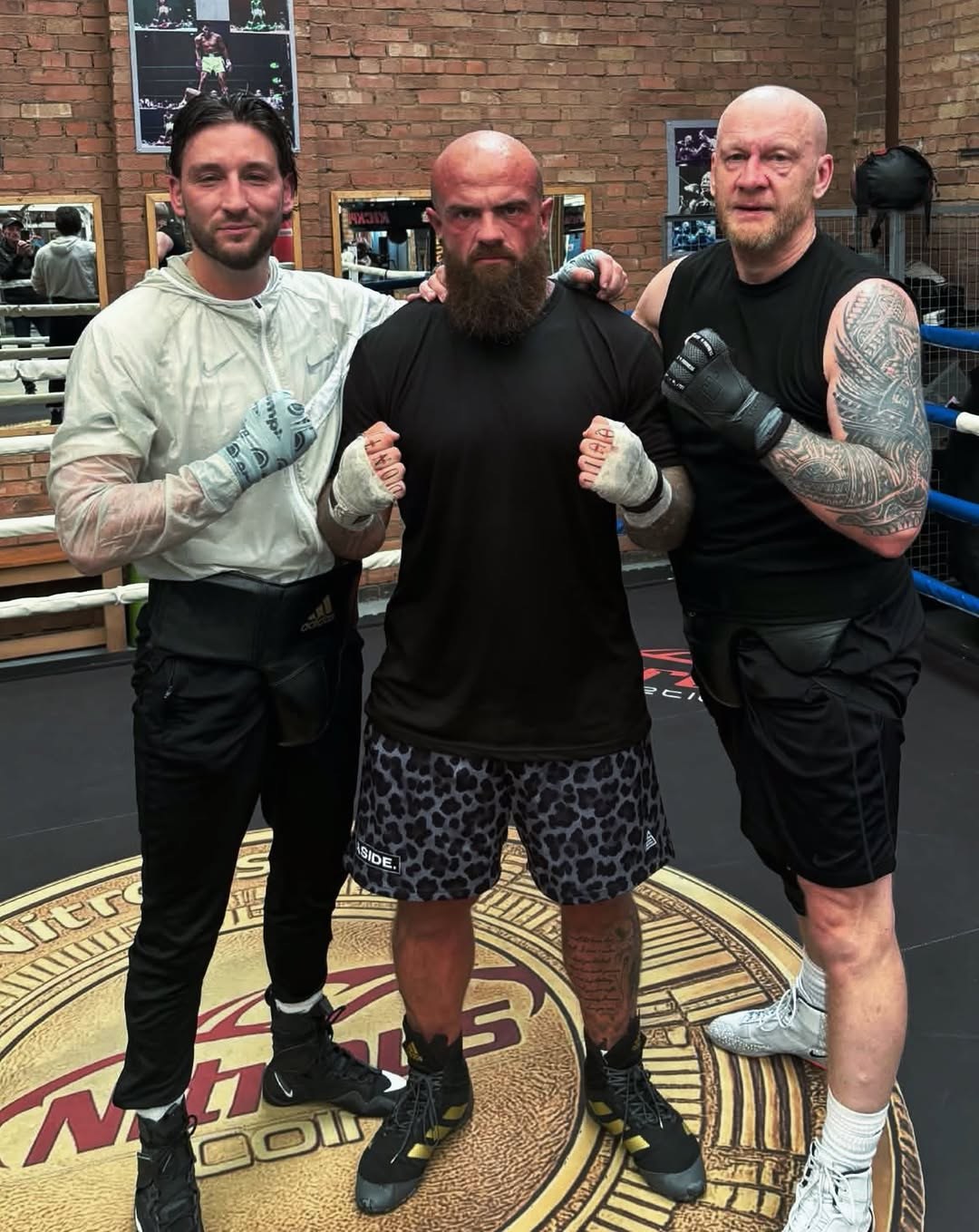 Three men standing in the boxing ring on the gym's logo canvas